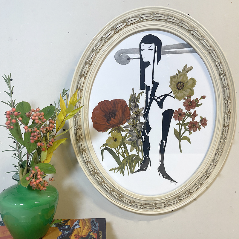 Handmade art combining screen printing and a collage of flowers depicting a woman pulling up her stocking while smoking in a upcycled white oval frame
