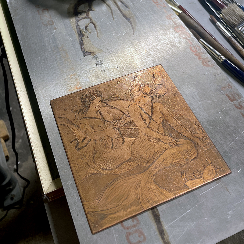 Handmade copper plate print of two mermaids putting fake shark fins on each other.